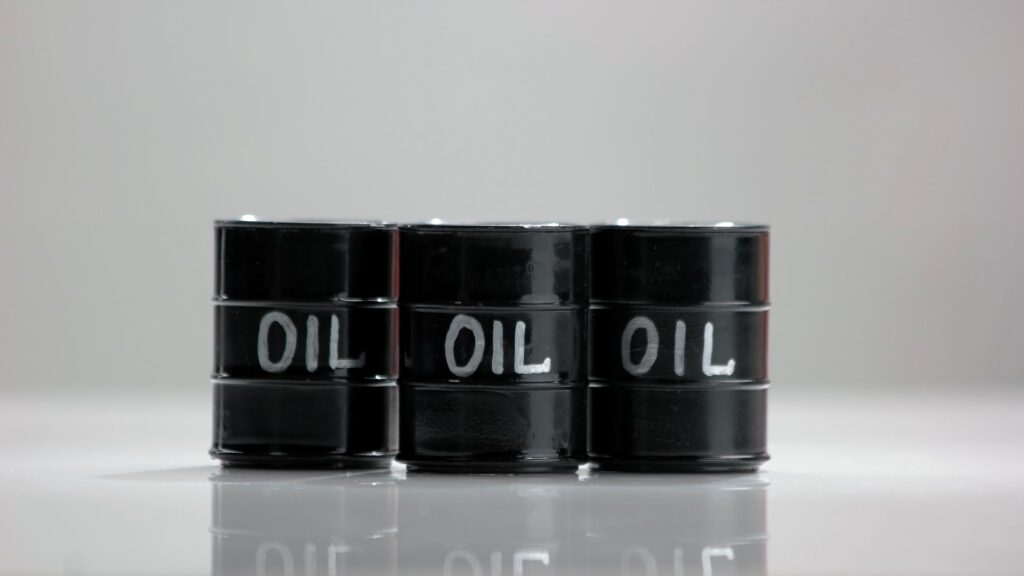 Three black oil barrels. White reflective surface. World economy concept.